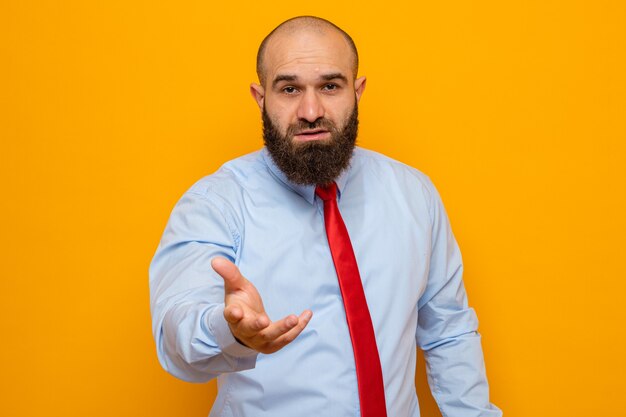 Hombre barbudo con corbata roja y camisa mirando levantando el brazo como si fuera a hacer una pregunta