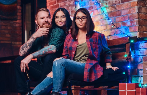 Un hombre barbudo y dos mujeres morenas celebran la fiesta de Navidad en una habitación con interior tipo loft.