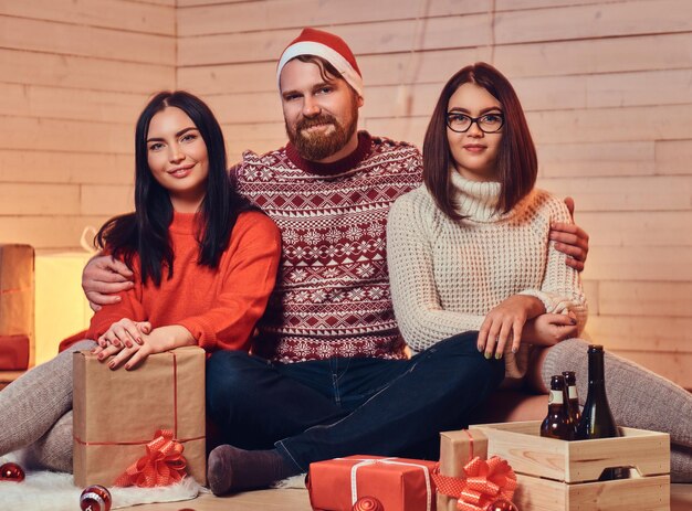 Un hombre barbudo y dos mujeres morenas fiesta de Navidad sobre una pared de madera blanca.