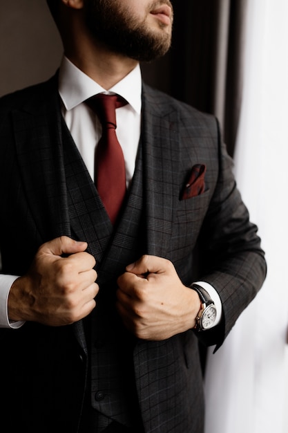 Hombre barbudo con elegante esmoquin y corbata roja, manos fuertes de hombre