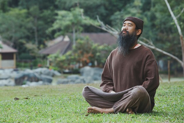 Un hombre barbudo está meditando sobre la hierba verde