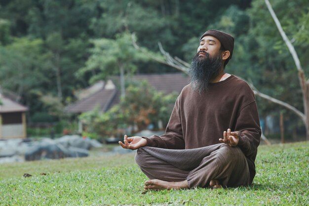 Un hombre barbudo está meditando sobre la hierba verde