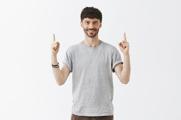 Hombre barbudo con estilo guapo apuntando con el dedo hacia arriba y sonriendo feliz