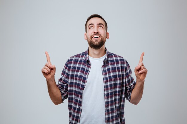 Hombre barbudo feliz en camisa apuntando hacia arriba