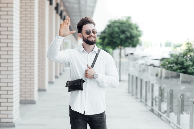 Un hombre barbudo, feliz, sonriente y elegante saluda con amigos en las calles de la ciudad cerca del moderno centro de oficinas