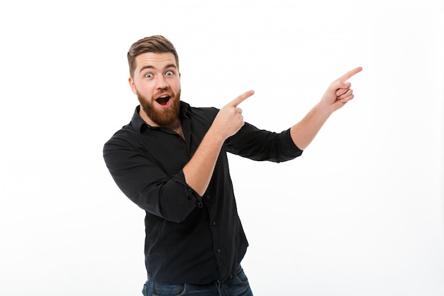 Foto gratuita hombre barbudo feliz sorprendido en camisa apuntando lejos