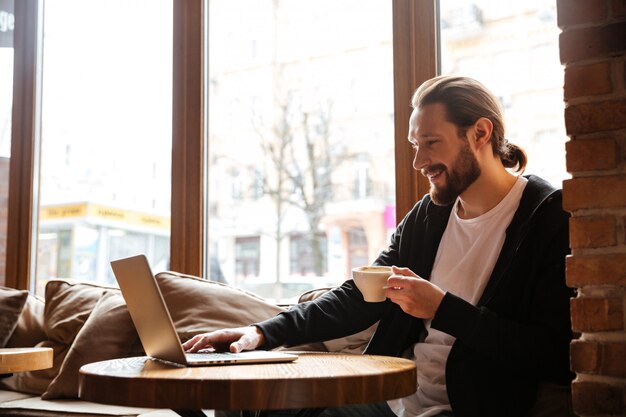 Hombre barbudo feliz usando laptop en café