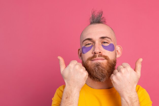 Hombre barbudo guapo europeo en camiseta amarilla y máscara de parches de ojos morados en rosa