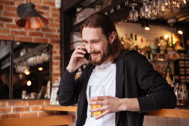 Hombre barbudo hablando por teléfono con una taza de cerveza