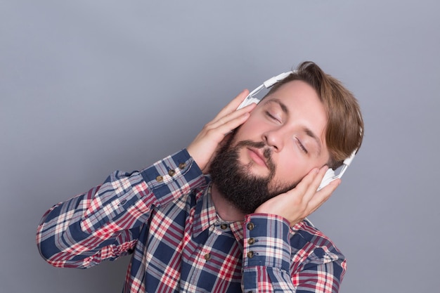 Hombre barbudo hipster disfrutando de diferentes pistas en auriculares escuchando la música haciendo feliz a este hombre aislado en gris