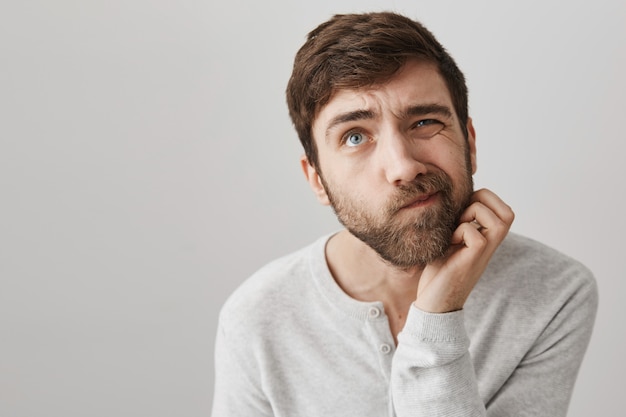 Hombre barbudo indeciso pensativo rascarse la barba y mirando hacia arriba pensando