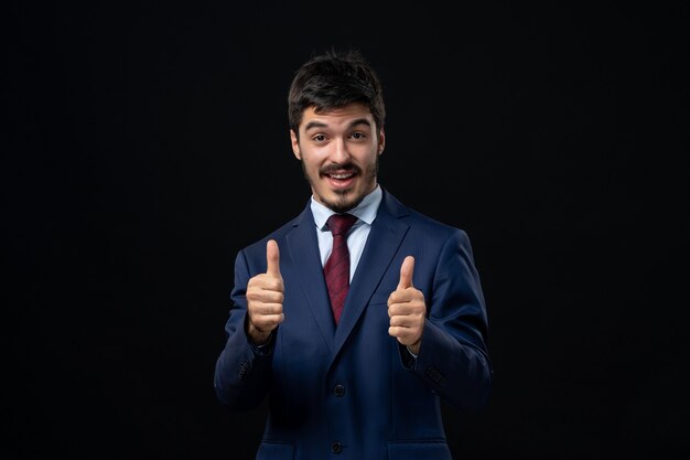 Hombre barbudo joven y emocional haciendo gesto bien con ambas manos en la pared oscura aislada