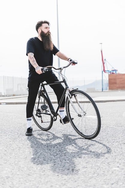 Hombre barbudo joven que se sienta en la bicicleta que mira lejos