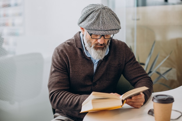 Hombre barbudo leyendo un libro y sentado a la mesa