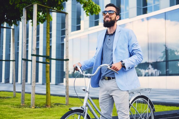 Hombre barbudo de lujo con gafas de sol en bicicleta en el centro.