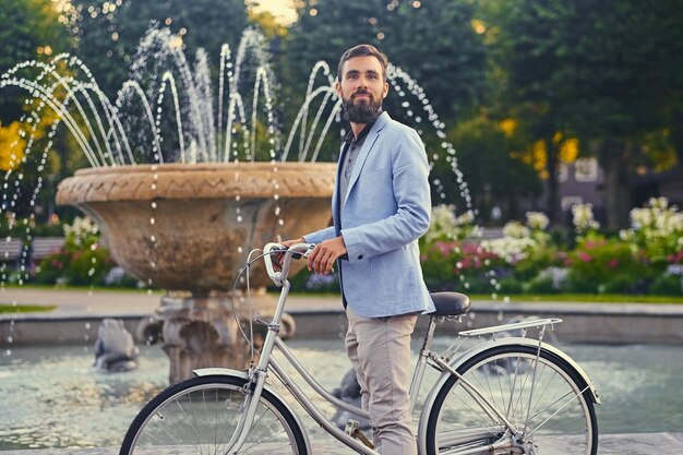 Hombre barbudo de lujo con gafas de sol en una bicicleta sobre el fondo de la fuente de la ciudad.