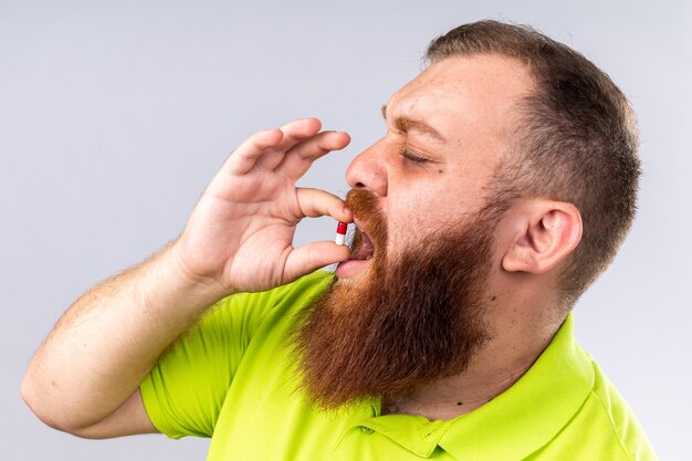 Hombre barbudo malsano en polo amarillo tomando medicamentos