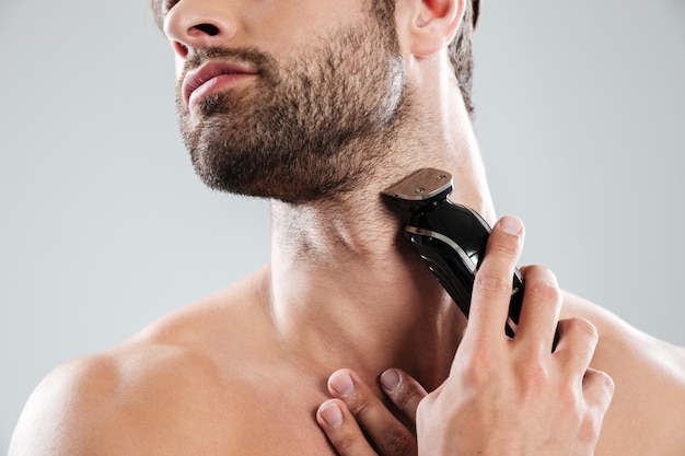 Hombre barbudo con maquinilla de afeitar eléctrica