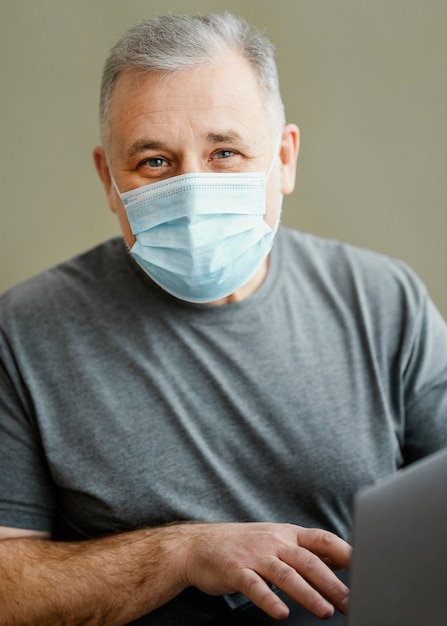 Hombre barbudo con mascarilla quirúrgica sosteniendo portátil