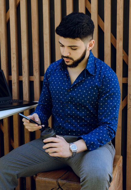 Hombre barbudo navegando por internet en un teléfono inteligente mientras descansa en un café durante el día