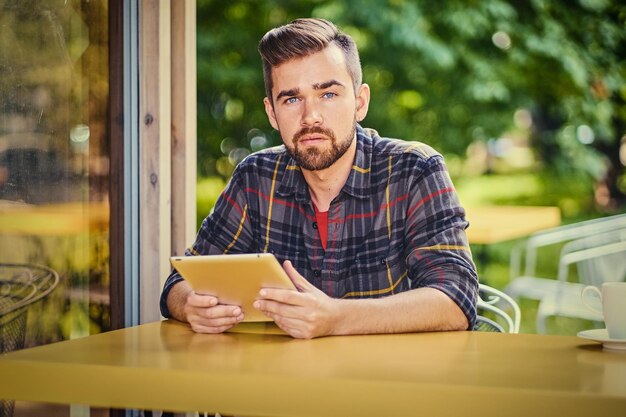 Hombre barbudo de ojos azules que usa una tableta en un café en una calle.