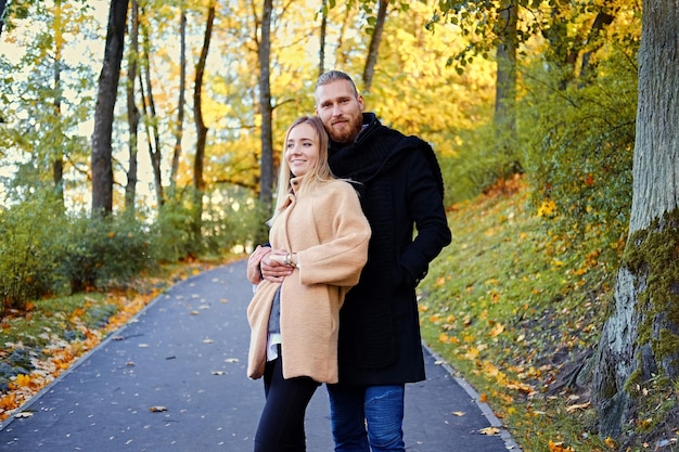 Hombre barbudo pelirrojo y mujer rubia linda posando en la carretera en un parque de otoño.