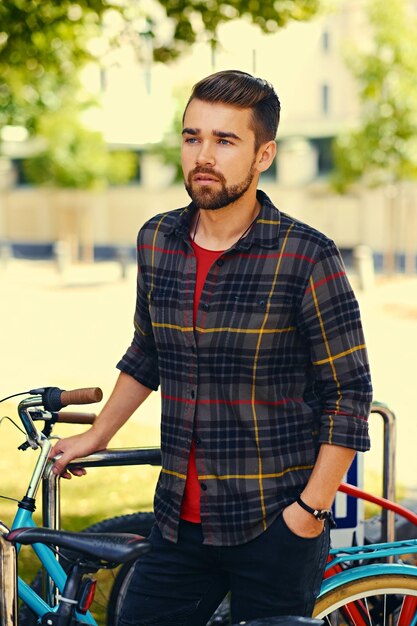 Un hombre barbudo positivo vestido con una camisa de lana cerca del estacionamiento de bicicletas.