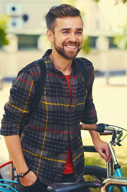 Un hombre barbudo positivo vestido con una camisa de lana cerca del estacionamiento de bicicletas.