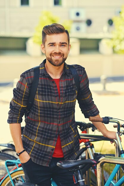 Un hombre barbudo positivo vestido con una camisa de lana cerca del estacionamiento de bicicletas.