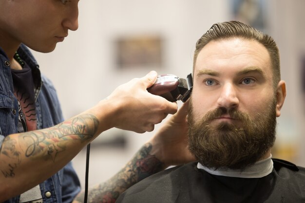 Hombre barbudo que consigue el corte de pelo en barbería