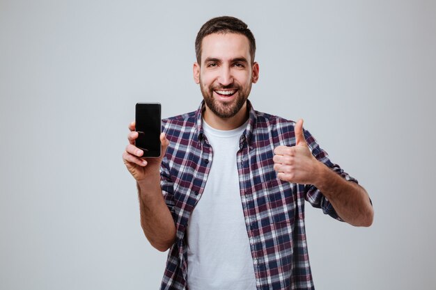 Hombre barbudo que muestra la pantalla del teléfono inteligente en blanco y pulgar arriba