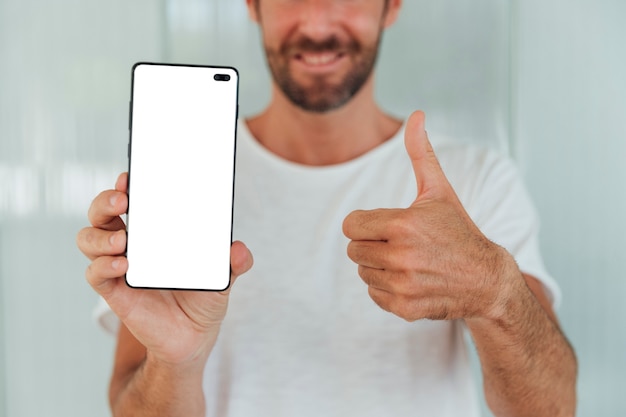 Hombre barbudo que muestra el teléfono con el pulgar hacia arriba