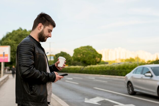 Hombre barbudo que sostiene la taza y el teléfono inteligente