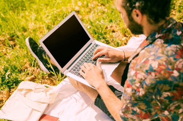 Hombre barbudo que trabaja en la computadora portátil en prado