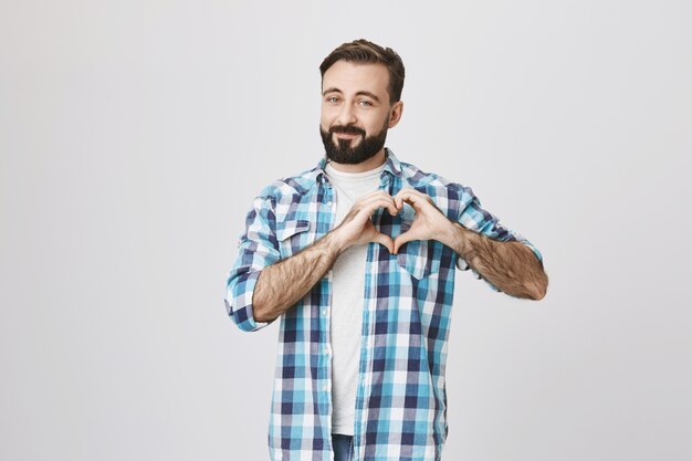 Hombre barbudo romántico que muestra el signo del corazón, expresa amor