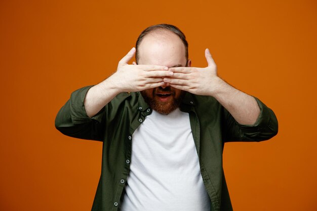 Hombre barbudo con ropa informal y gafas que cubren los ojos con las manos sobre fondo naranja