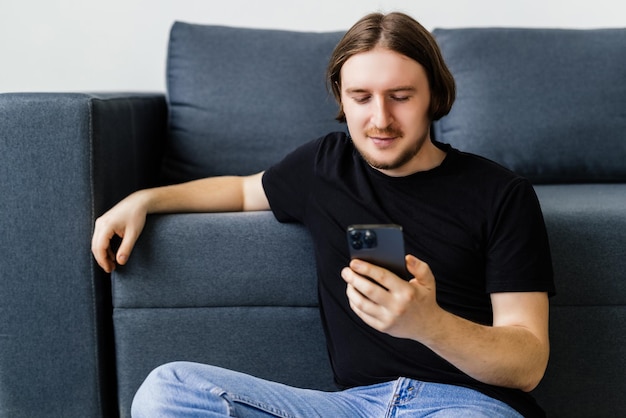 Hombre barbudo seguro está sentado en el sofá y escribiendo en el teléfono inteligente