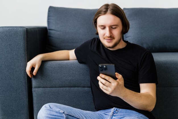 Hombre barbudo seguro está sentado en el sofá y escribiendo en el teléfono inteligente