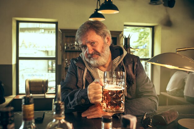 El hombre barbudo senior bebiendo cerveza en el pub