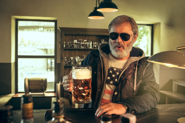 El hombre barbudo senior bebiendo cerveza en pub