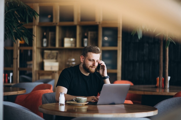 Hombre barbudo sentado en un café tomando café y trabajando en una computadora