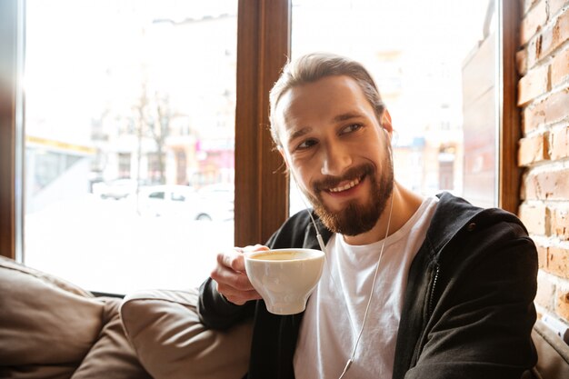 Hombre barbudo sonriente en café cerca de la ventana