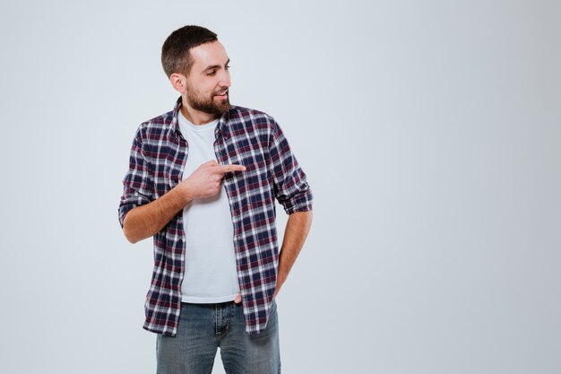 Hombre barbudo sonriente en camisa apuntando lejos