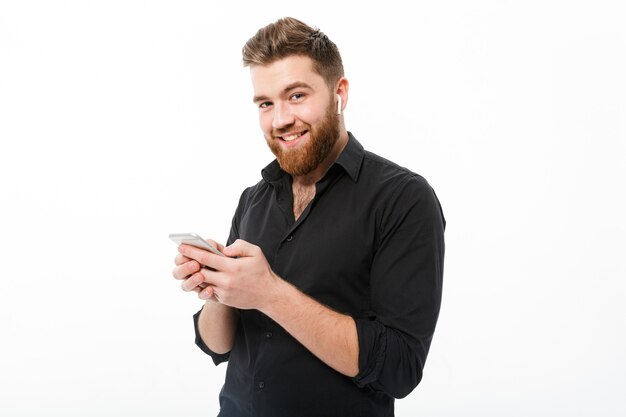 Hombre barbudo sonriente en camisa con smartphone