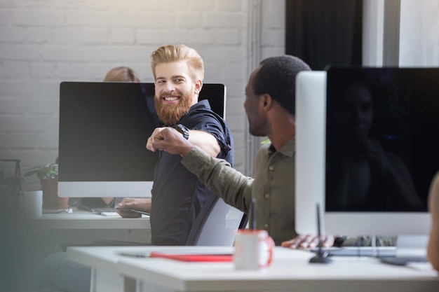 Hombre barbudo sonriente dando un golpe de puño a un colega masculino