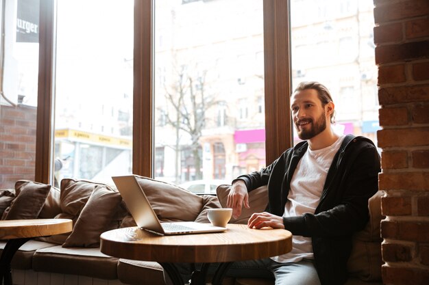 Hombre barbudo sonriente junto a la mesa con laptop