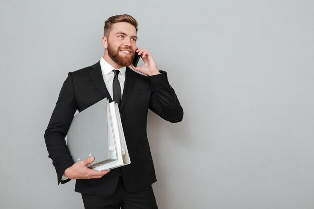 Hombre barbudo sonriente en traje hablando por teléfono