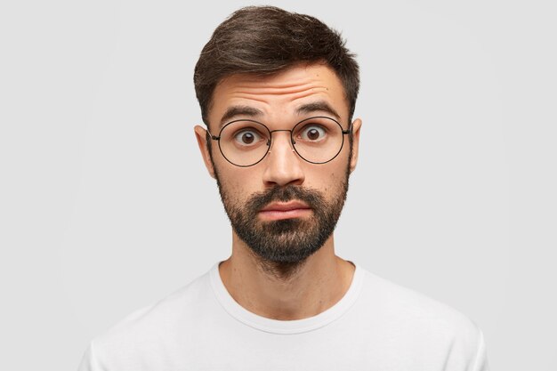 Hombre barbudo sorprendido con barba espesa y bigote, mira con expresión de asombro después de escuchar noticias de terror