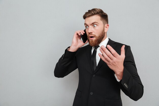 Hombre barbudo sorprendido hablando por su teléfono y mirando a otro lado