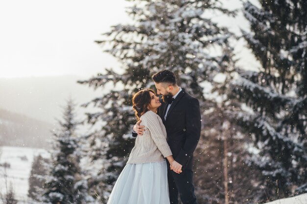Hombre barbudo y su novia encantadora posan en la nieve en un bosque de invierno mágico